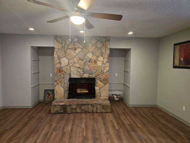 unfurnished living room with a textured ceiling, dark hardwood / wood-style floors, a stone fireplace, and ceiling fan