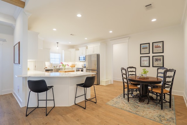 kitchen featuring light wood finished floors, appliances with stainless steel finishes, a breakfast bar, a peninsula, and crown molding