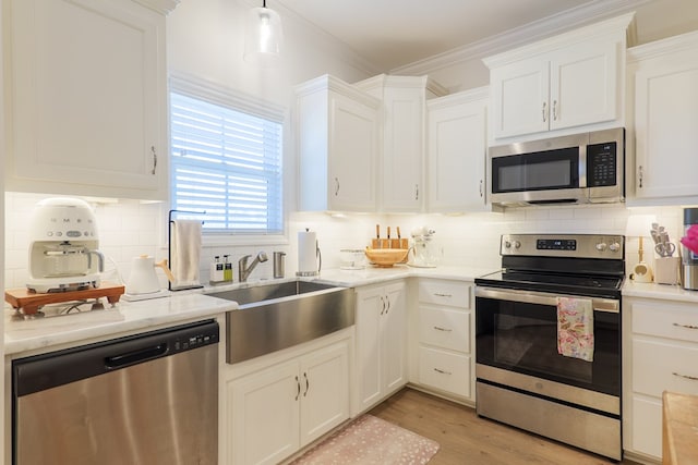 kitchen with light wood-style flooring, stainless steel appliances, a sink, white cabinets, and ornamental molding