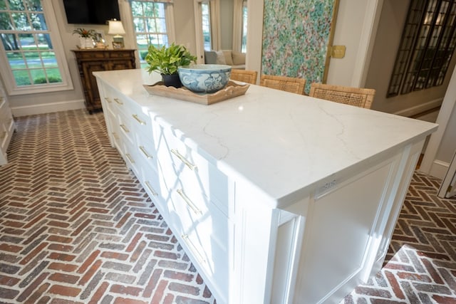 793 Lake Laurie Dr, Valdosta, GA 31605 - kitchen featuring a kitchen island, white cabinetry, light stone countertops, brick floor, and baseboards