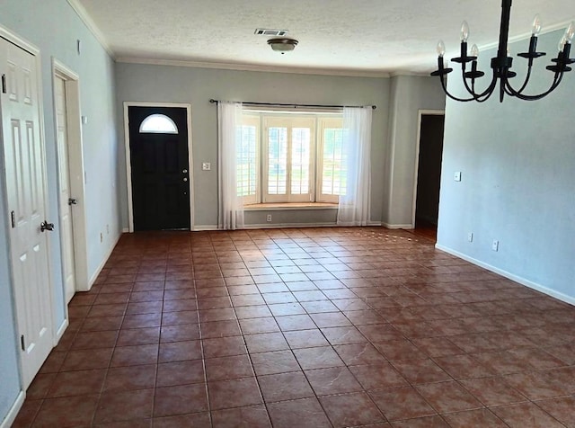 entrance foyer with dark tile patterned floors, ornamental molding, a textured ceiling, and an inviting chandelier