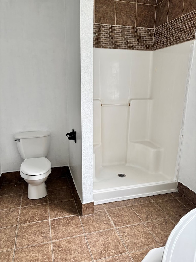 bathroom with toilet, tile patterned flooring, and tiled shower