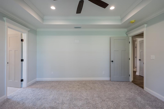 spare room with a tray ceiling, crown molding, and light colored carpet