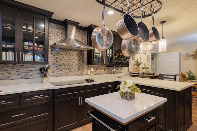 kitchen featuring a kitchen island, decorative light fixtures, crown molding, black electric cooktop, and wall chimney exhaust hood