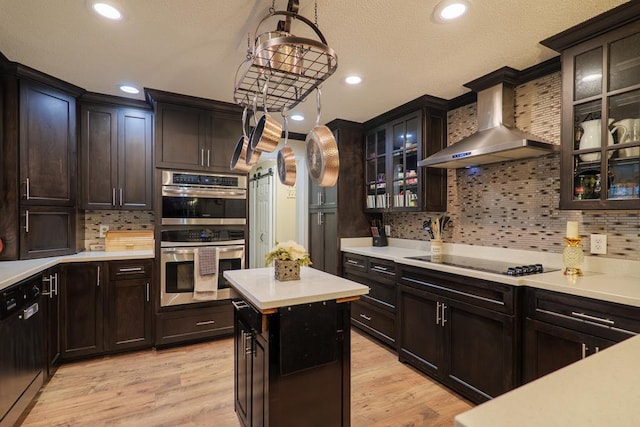 kitchen with pendant lighting, wall chimney range hood, black appliances, and light wood-type flooring