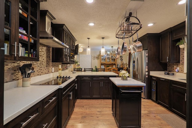 kitchen with decorative light fixtures, a center island, stainless steel fridge, kitchen peninsula, and wall chimney range hood