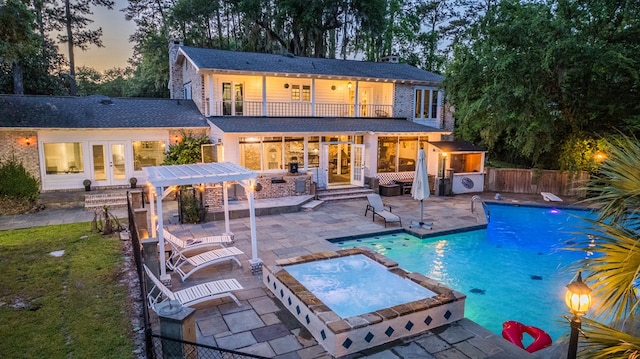 pool at dusk featuring an in ground hot tub and a patio area