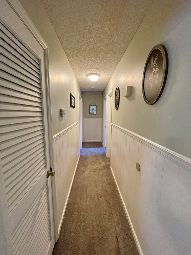 hallway featuring wainscoting, a textured ceiling, and carpet
