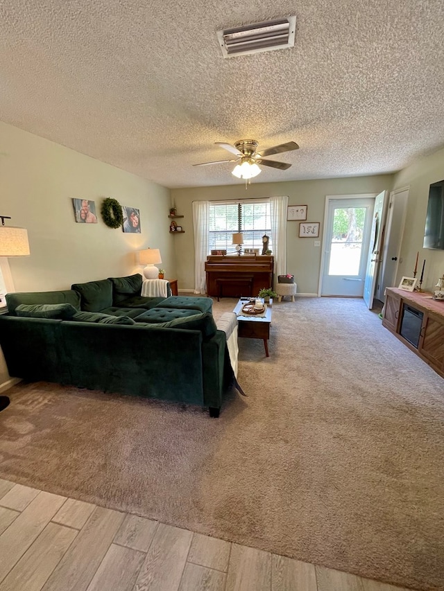 living area featuring a textured ceiling, visible vents, a ceiling fan, and light wood-style floors