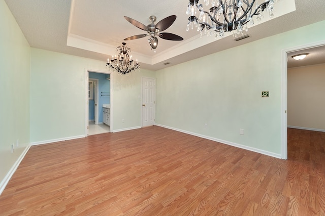 empty room with light hardwood / wood-style flooring, a tray ceiling, ornamental molding, a textured ceiling, and ceiling fan with notable chandelier