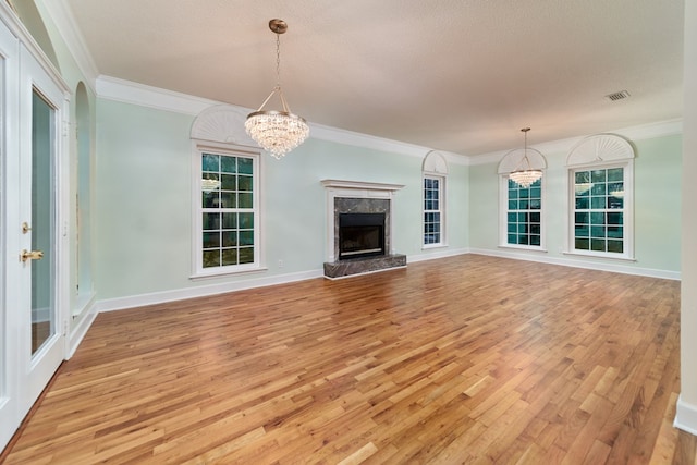 unfurnished living room with ornamental molding, a high end fireplace, a chandelier, and light hardwood / wood-style flooring