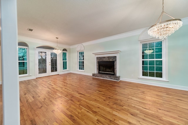 unfurnished living room with a chandelier, a high end fireplace, crown molding, a textured ceiling, and light hardwood / wood-style flooring