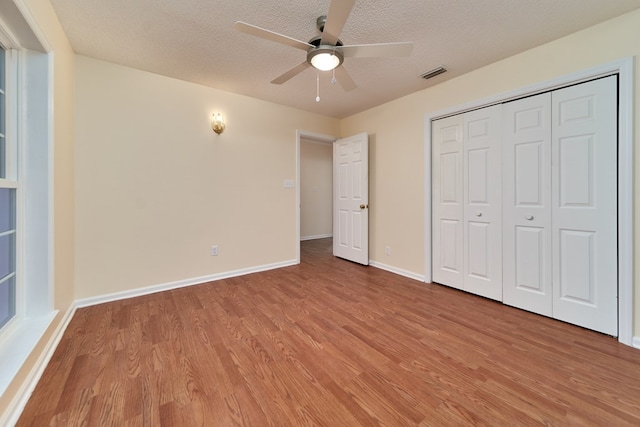 unfurnished bedroom with ceiling fan, light hardwood / wood-style floors, a closet, and a textured ceiling