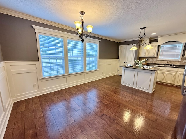 kitchen featuring sink, a center island, ornamental molding, hanging light fixtures, and a notable chandelier