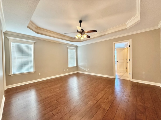 unfurnished room with ceiling fan, a tray ceiling, crown molding, and dark wood-type flooring