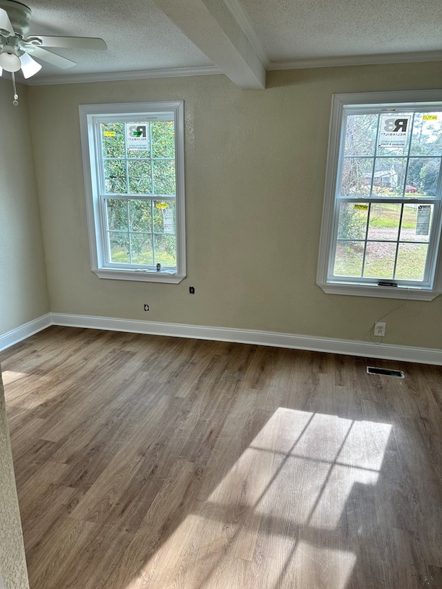 empty room featuring ceiling fan, plenty of natural light, beamed ceiling, and a textured ceiling