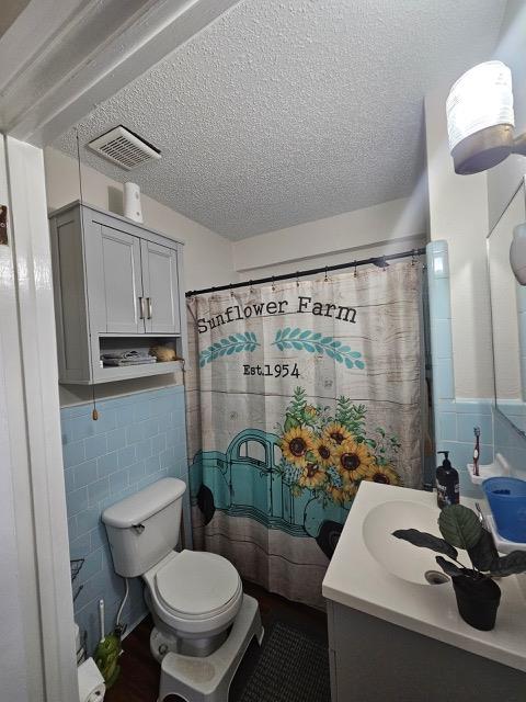 bathroom with vanity, tile walls, a textured ceiling, and toilet