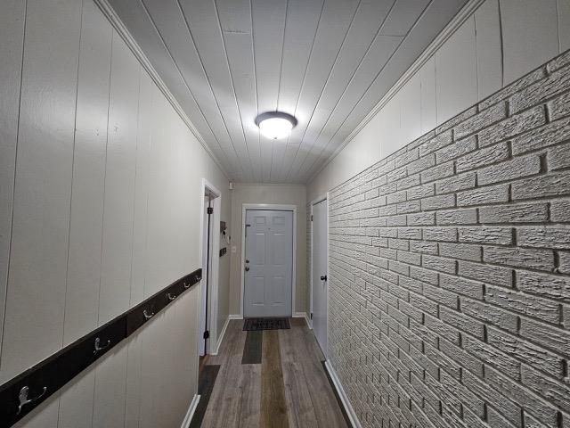 corridor with dark wood-type flooring, ornamental molding, wooden ceiling, and brick wall