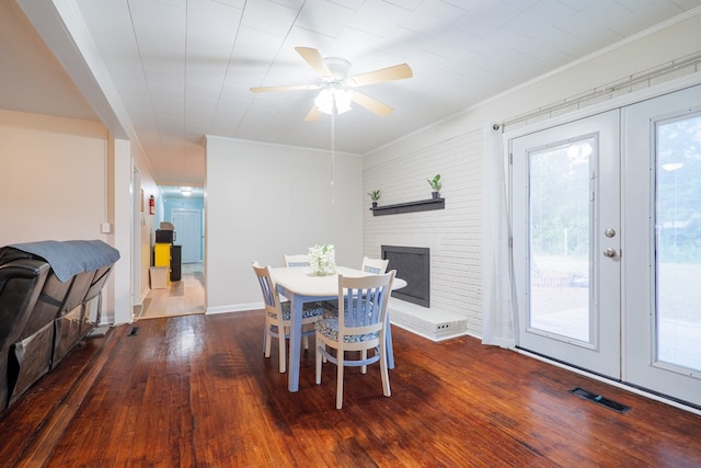 dining area featuring ceiling fan, crown molding, a brick fireplace, dark wood-type flooring, and french doors