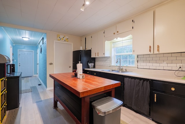 kitchen with sink, white cabinetry, backsplash, black refrigerator, and light hardwood / wood-style floors