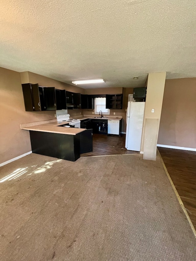 kitchen featuring white appliances, a peninsula, a sink, light countertops, and dark cabinets