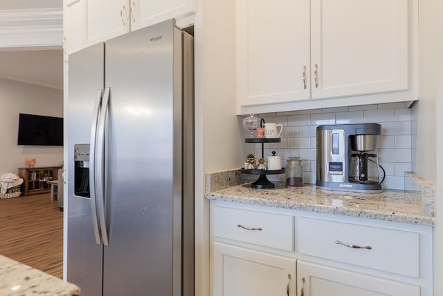 kitchen with crown molding, white cabinetry, light stone countertops, stainless steel fridge with ice dispenser, and decorative backsplash