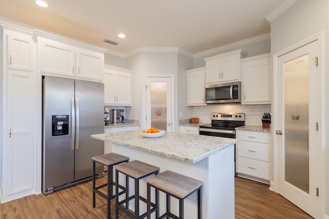 kitchen with white cabinetry, appliances with stainless steel finishes, a kitchen island, and light stone counters