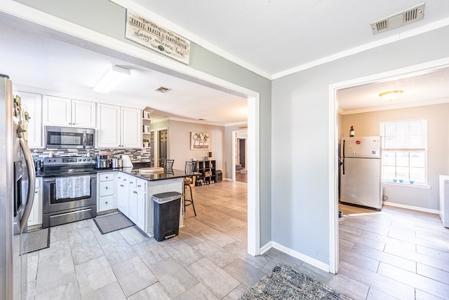 kitchen featuring stainless steel appliances, kitchen peninsula, decorative backsplash, and white cabinets