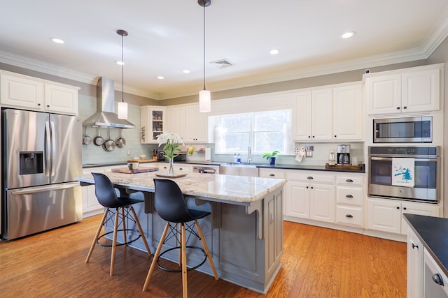 kitchen with appliances with stainless steel finishes, crown molding, light wood-style floors, and wall chimney range hood