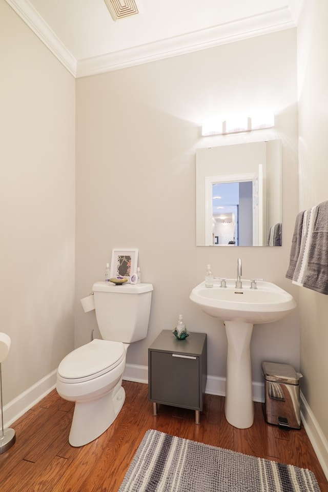 half bathroom featuring visible vents, toilet, ornamental molding, wood finished floors, and baseboards