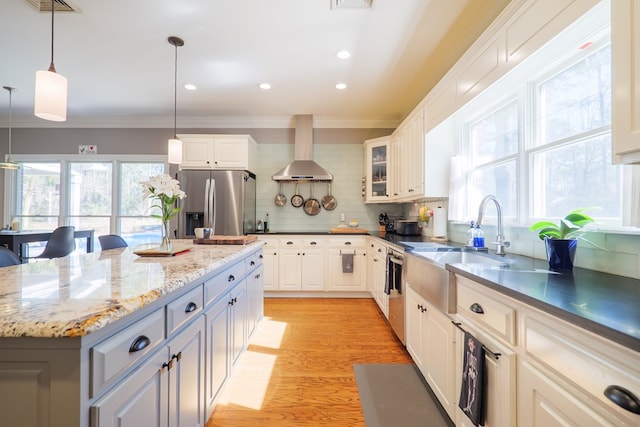 kitchen with light wood-style flooring, stainless steel appliances, wall chimney range hood, tasteful backsplash, and crown molding