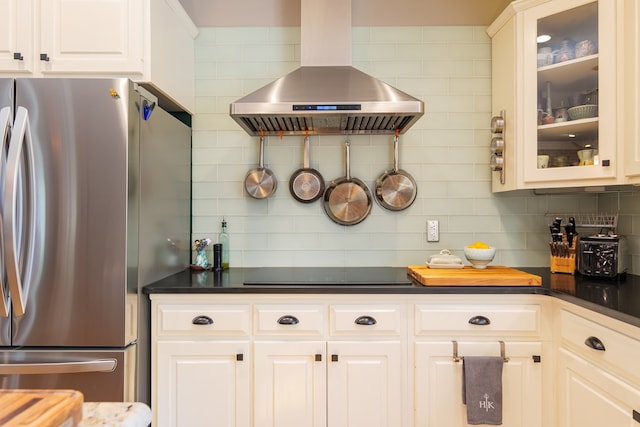 kitchen with tasteful backsplash, glass insert cabinets, freestanding refrigerator, black electric stovetop, and wall chimney range hood