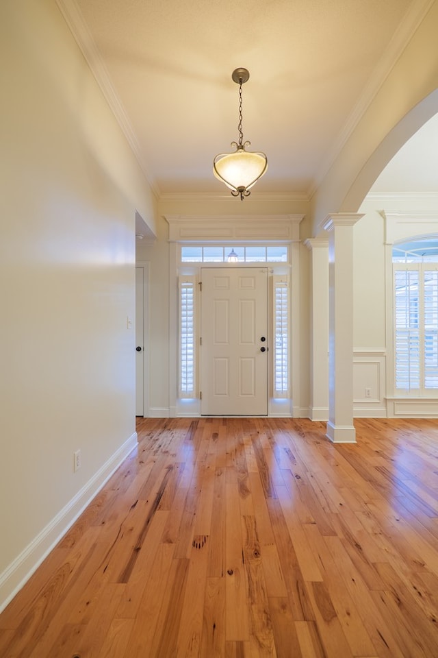 foyer entrance featuring arched walkways, decorative columns, light wood finished floors, ornamental molding, and baseboards