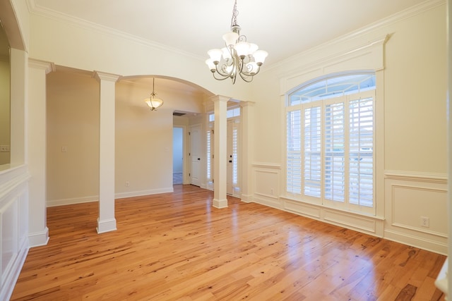 unfurnished dining area with arched walkways, a decorative wall, ornamental molding, light wood finished floors, and decorative columns