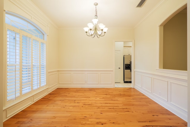 unfurnished dining area featuring visible vents, light wood-style flooring, ornamental molding, an inviting chandelier, and a decorative wall