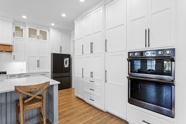 kitchen featuring white cabinets, a kitchen bar, light wood-type flooring, and black appliances