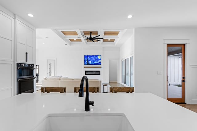 kitchen featuring coffered ceiling, sink, ceiling fan, double oven, and wood-type flooring