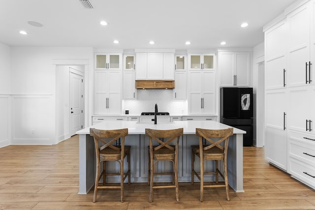 kitchen featuring black refrigerator, a kitchen bar, white cabinetry, and a kitchen island with sink