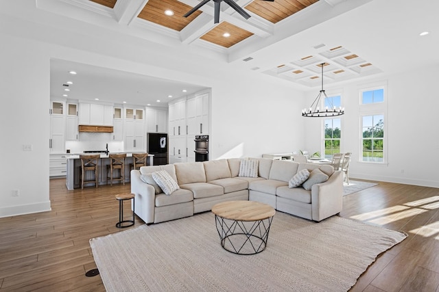 living room featuring light hardwood / wood-style flooring, ceiling fan with notable chandelier, and coffered ceiling