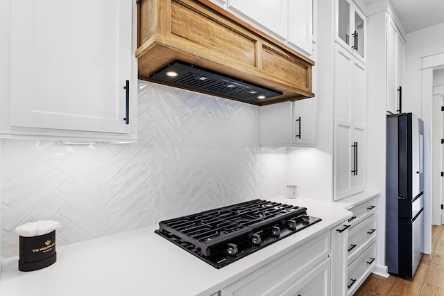 kitchen with decorative backsplash, custom range hood, black appliances, light hardwood / wood-style flooring, and white cabinets