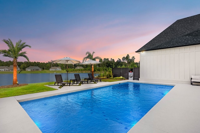 pool at dusk with a patio area and a water view