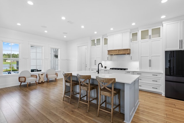 kitchen featuring black refrigerator, a kitchen bar, light wood-type flooring, white cabinets, and an island with sink