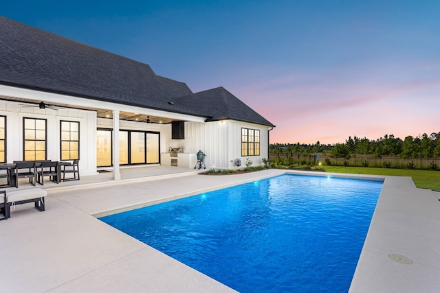 pool at dusk with ceiling fan and a patio