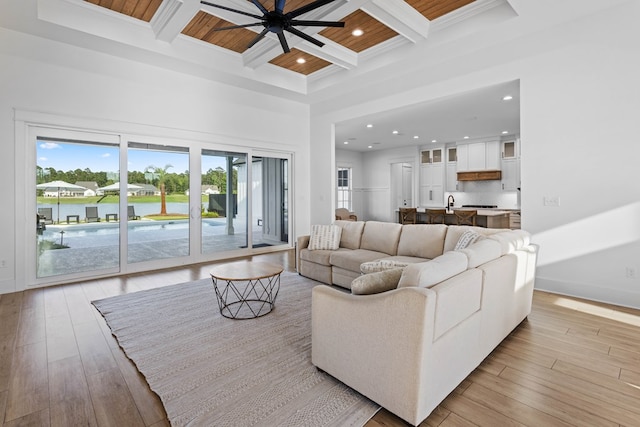 living room featuring coffered ceiling, ceiling fan, light wood-type flooring, ornamental molding, and beam ceiling