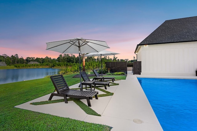 pool at dusk with a yard, a water view, and a patio