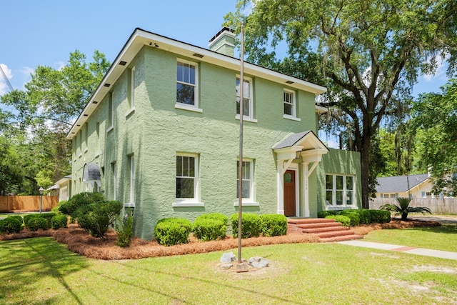 view of front of property featuring a front lawn, fence, a chimney, and stucco siding