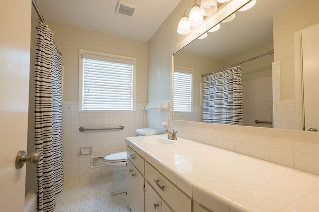 bathroom featuring tile patterned floors, vanity, tile walls, toilet, and walk in shower