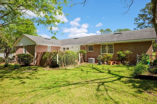 rear view of house with central AC unit and a yard