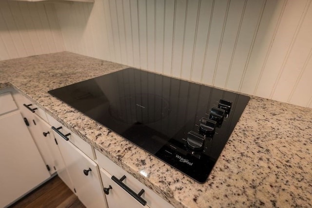 room details with white cabinetry, dark hardwood / wood-style flooring, black electric cooktop, and light stone countertops