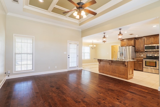 kitchen with a breakfast bar, a center island with sink, ornamental molding, stainless steel appliances, and light hardwood / wood-style floors